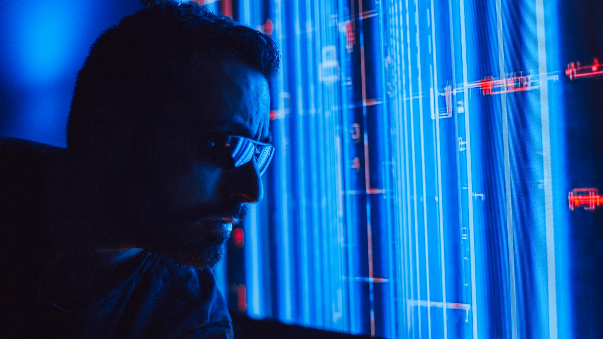 A man in sunglasses intently studies a vibrant blue holographic screen, symbolizing digital technology.